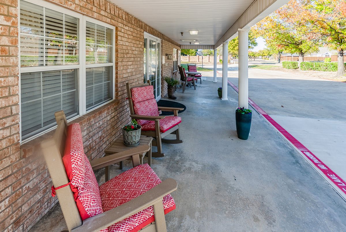 A cozy porch with red-cushioned chairs and potted plants along a brick building.