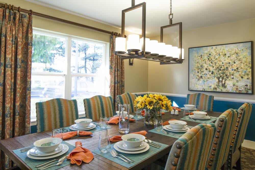 A dining room featuring a set table with striped chairs, a modern chandelier, and decorative flowers.