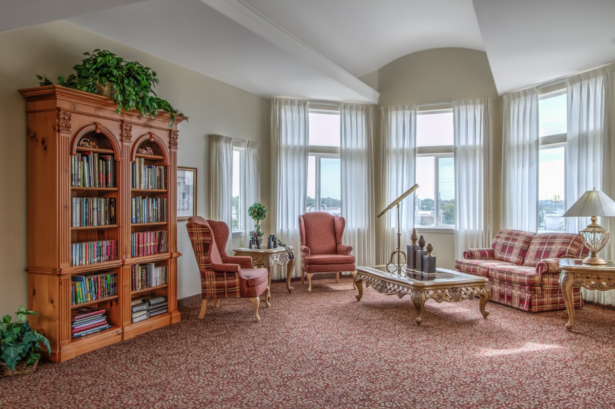 A cozy living room with armchairs, a coffee table, and a bookshelf against large windows.