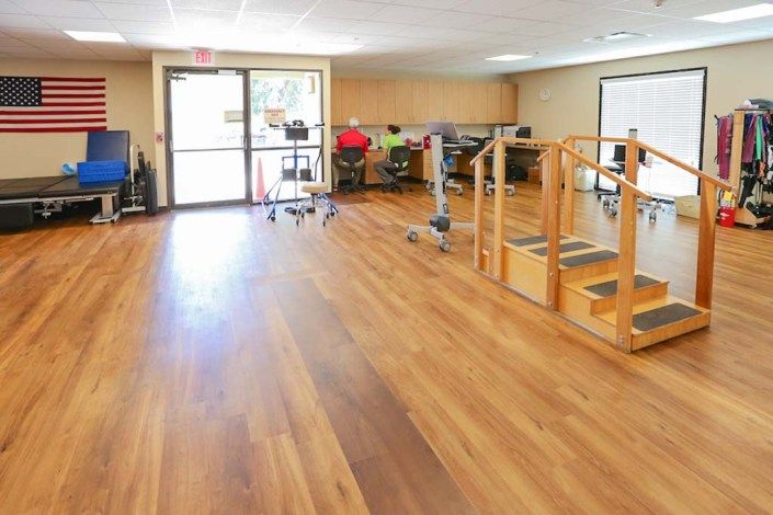 A spacious physical therapy room with wooden flooring and various exercise equipment.