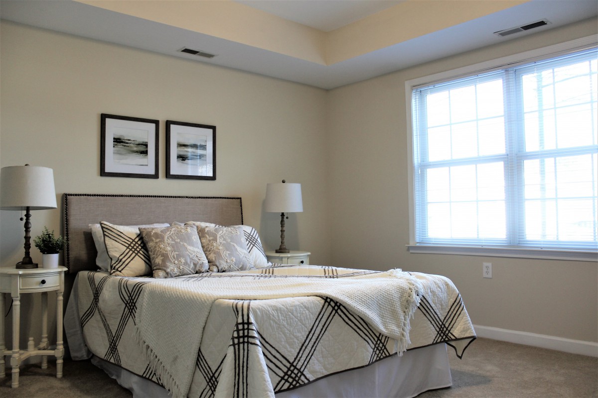 A minimalist bedroom with a neatly made bed, two framed pictures, and a lamp by the window.