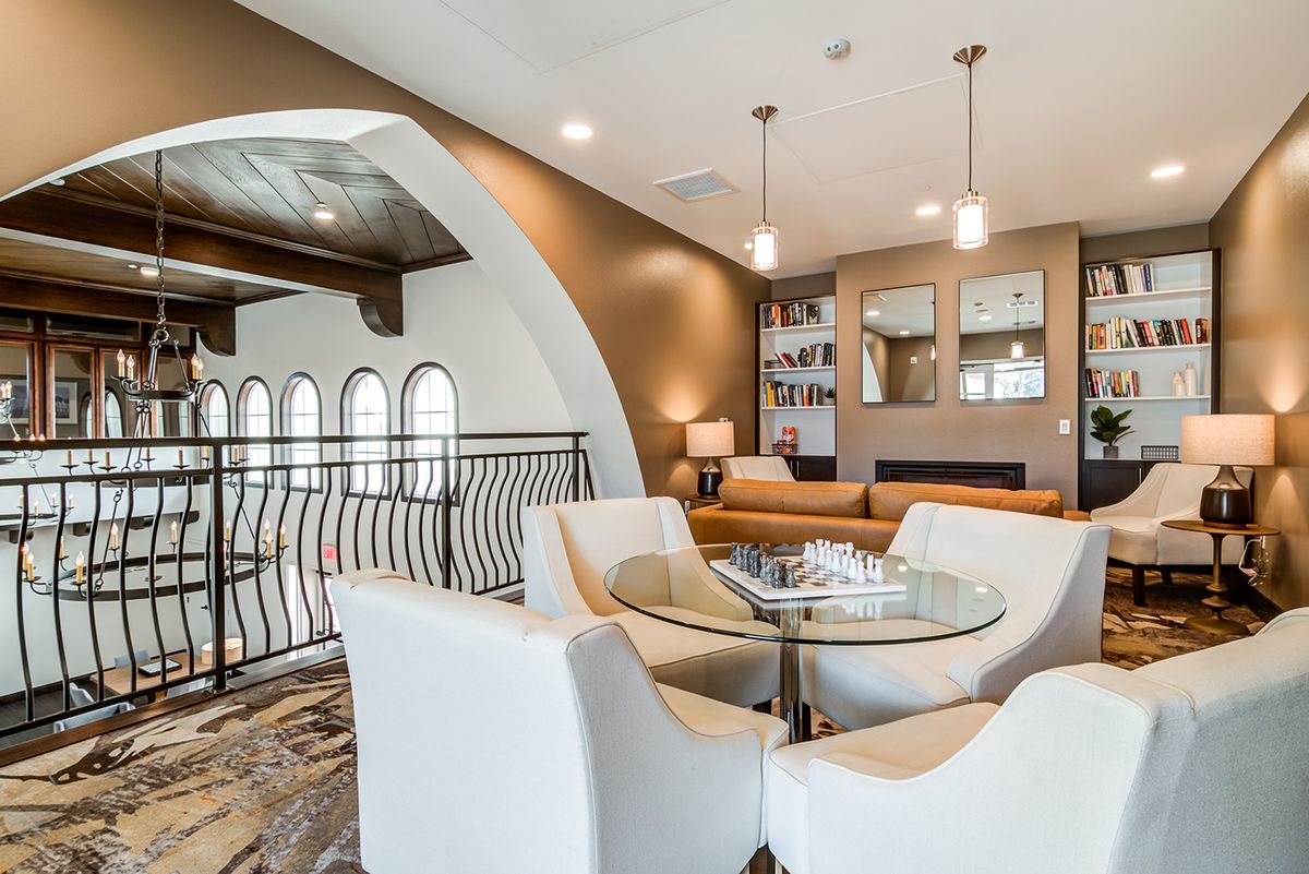 A modern living room with a stylish seating area featuring white armchairs around a glass table, complemented by elegant lighting and decorative wall design.