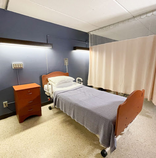 A clean and organized hospital patient room featuring a bed, nightstand, and curtains for privacy.
