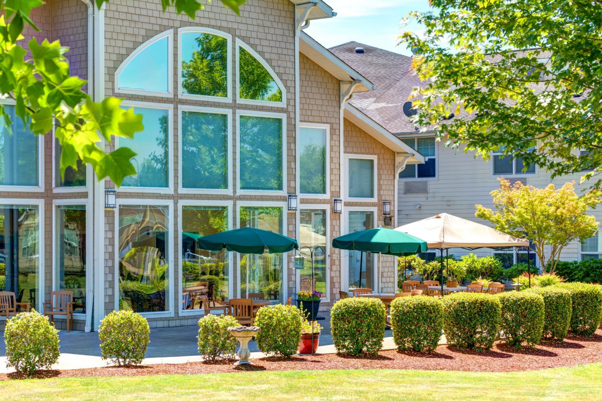 A modern house with large windows opening to a well-maintained garden and patio on a sunny day.
