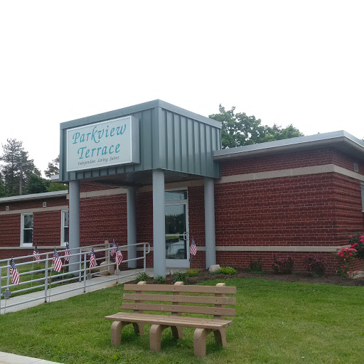 Exterior view of a modern brick building with a sign, featuring a seating area in front.