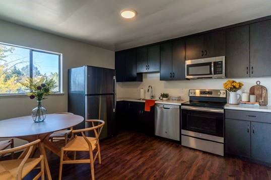A modern kitchen with black cabinets, stainless steel appliances, and a wooden dining set.