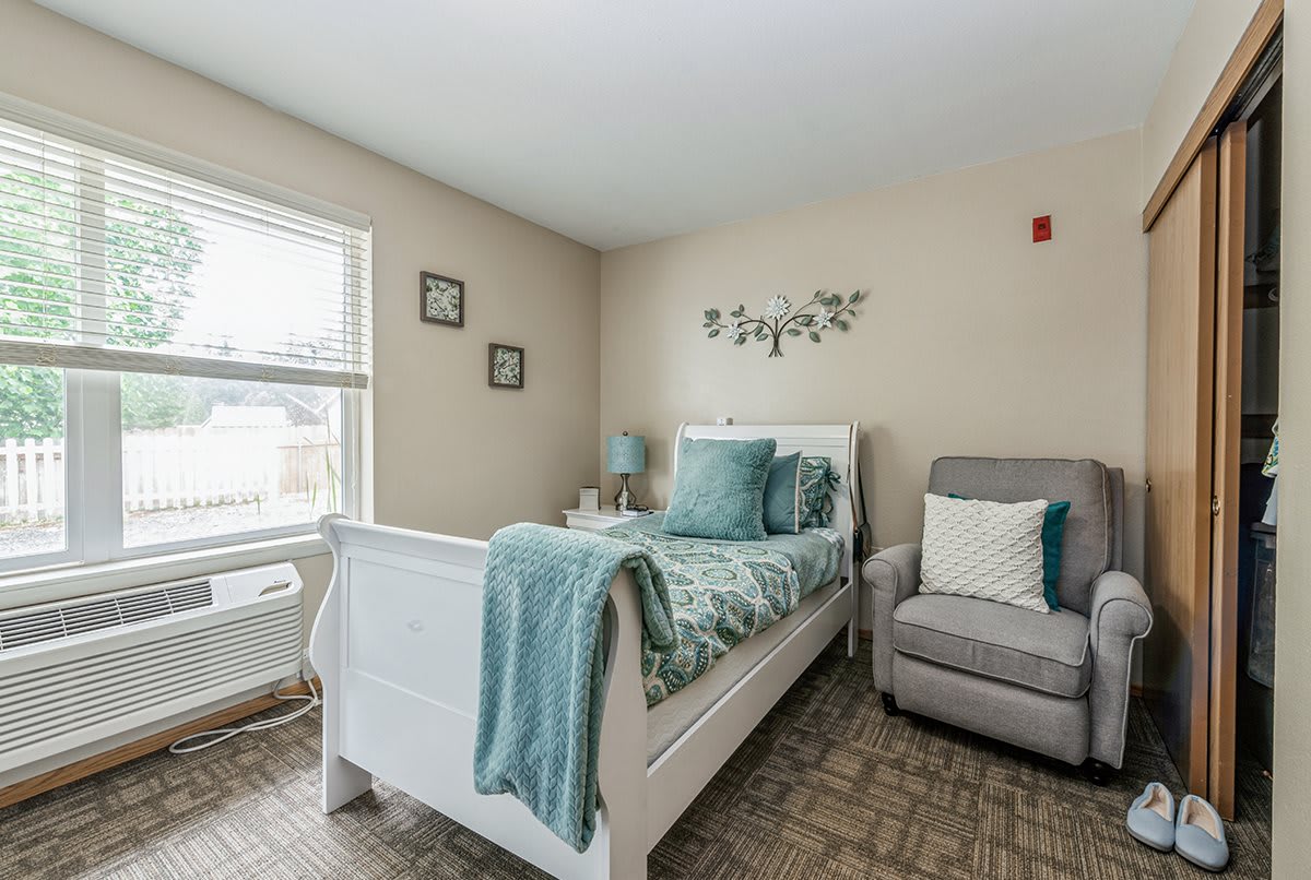 A cozy bedroom with a single bed, an armchair, and soft lighting.