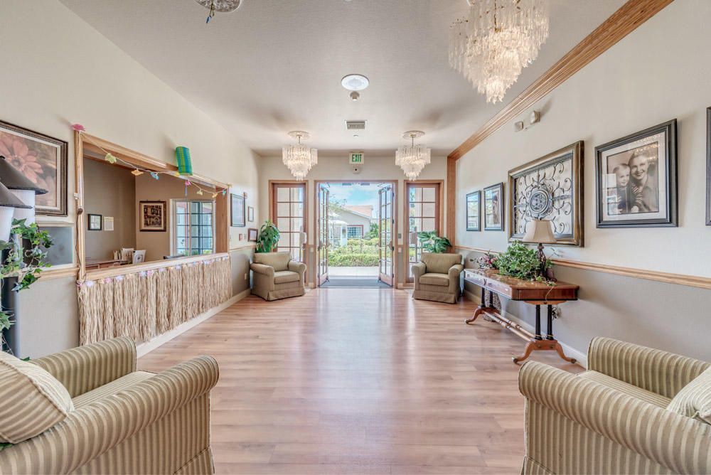 A bright and elegant lobby area with chandeliers, armchairs, and a wooden floor.