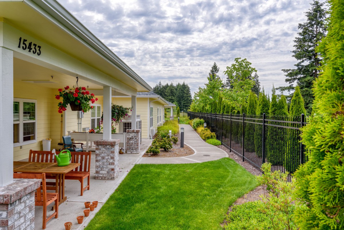A beautifully landscaped backyard with a patio and outdoor furniture, showcasing a lush green lawn and a pathway lined with plants.