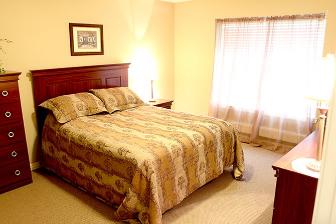 A cozy bedroom with a bed, nightstand, lamp, and window with curtains.