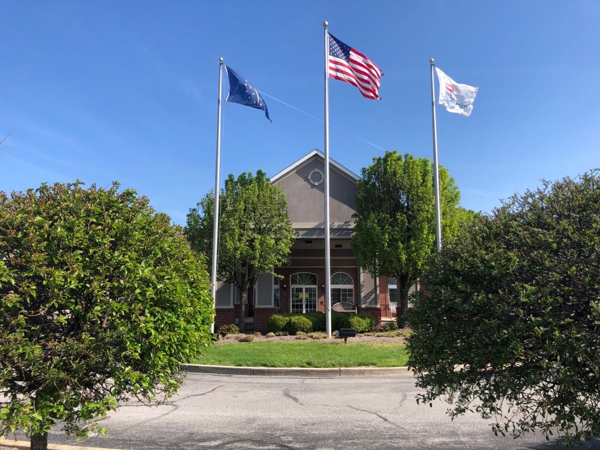 A building with three flags and surrounding greenery under a clear blue sky.