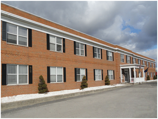 A brick building featuring multiple windows and a welcoming front entrance, set against a cloudy sky.