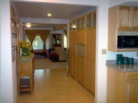 A view from the kitchen into a hallway leading to the living room, featuring wooden cabinetry and modern decor.