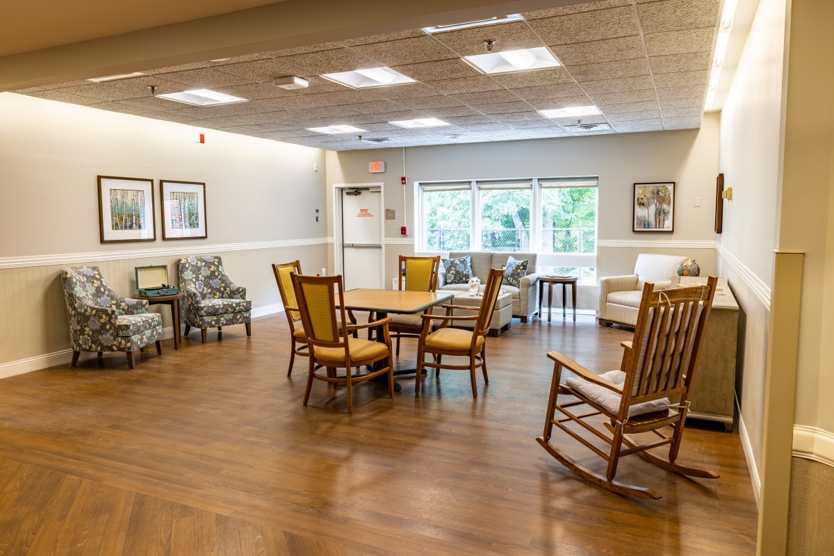 A spacious and well-lit common area featuring various seating options and tables with wooden flooring.