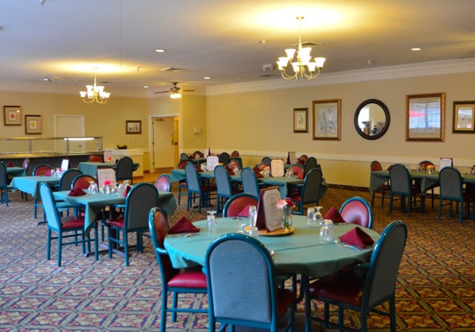 A spacious dining room with neatly arranged tables and chairs, illuminated by elegant chandeliers.