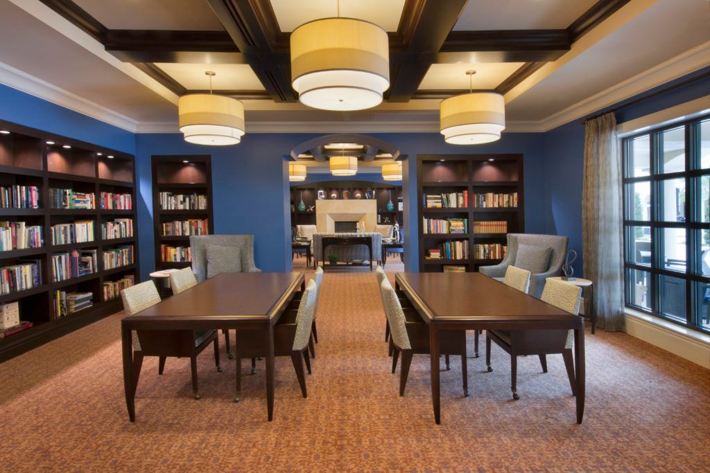 A cozy library reading room with bookshelves, tables, and chairs under warm lighting.