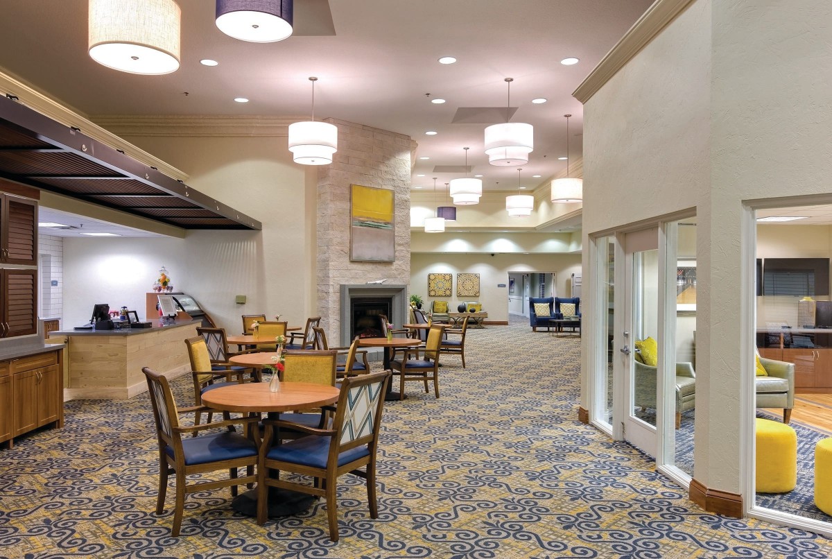 A modern dining area with tables and chairs, featuring stylish lighting and carpeted flooring.