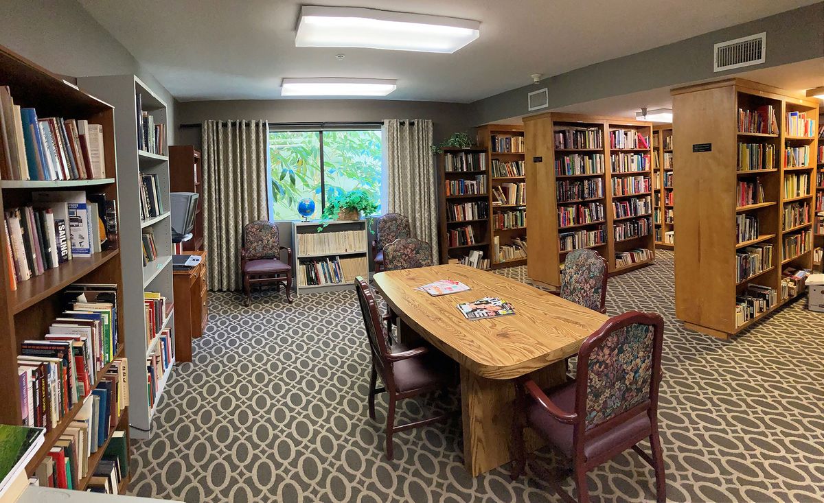 A cozy library room with bookshelves, a wooden table, and chairs near a window.