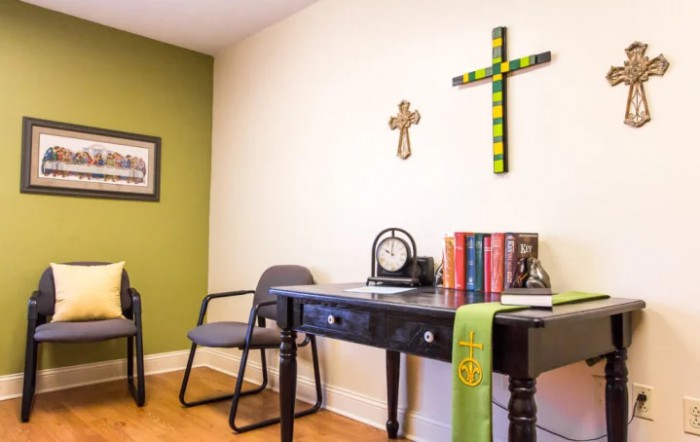 A small office space with a desk, chairs, and religious decor on the walls.
