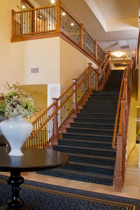 A carpeted staircase with wooden railings in a well-lit interior space, featuring a decorative vase with flowers.