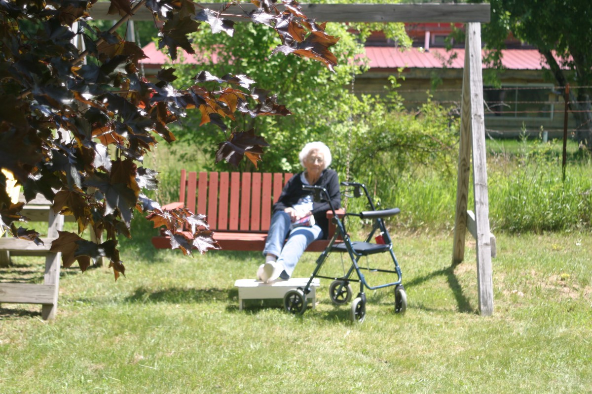 An elderly person sitting on a bench outdoors with a walker nearby.
