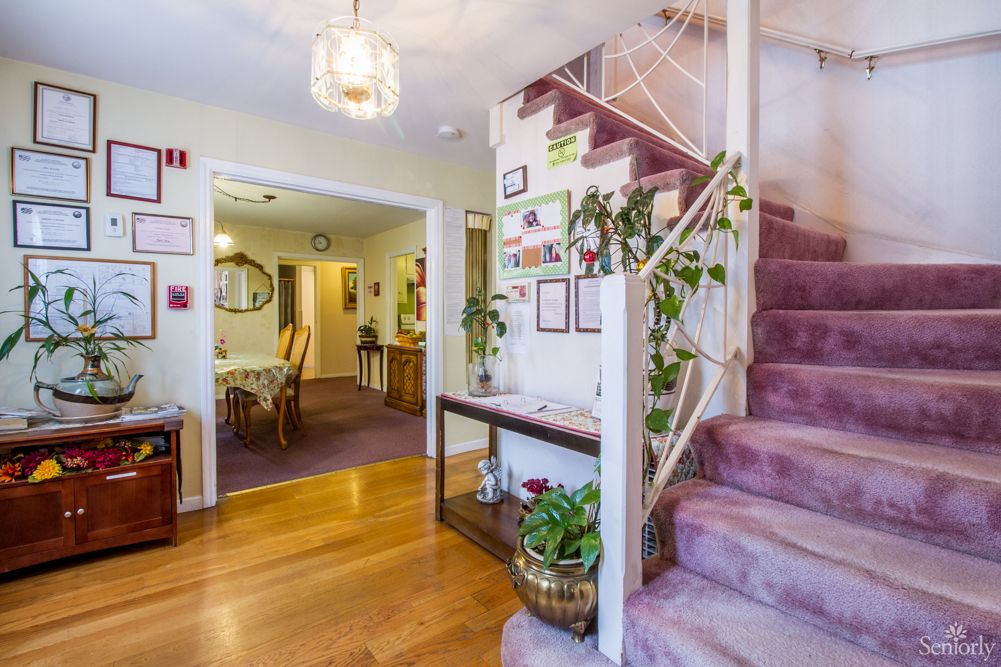 A cozy home interior showcases a staircase with pink carpet and vibrant plants, leading to a warmly lit dining area.