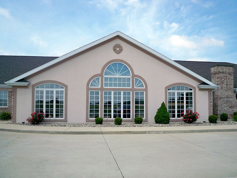 A symmetrical building facade with large windows and neatly trimmed shrubs under a partly cloudy sky.