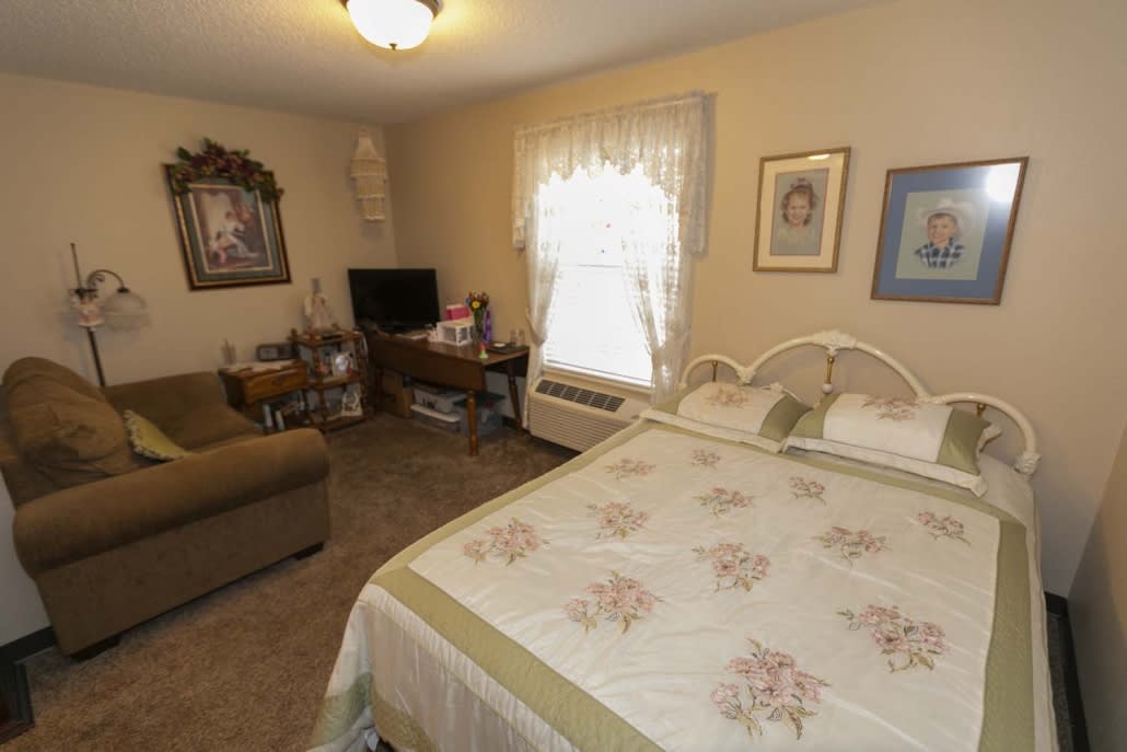 A cozy bedroom with a bed, sofa, desk, and television.