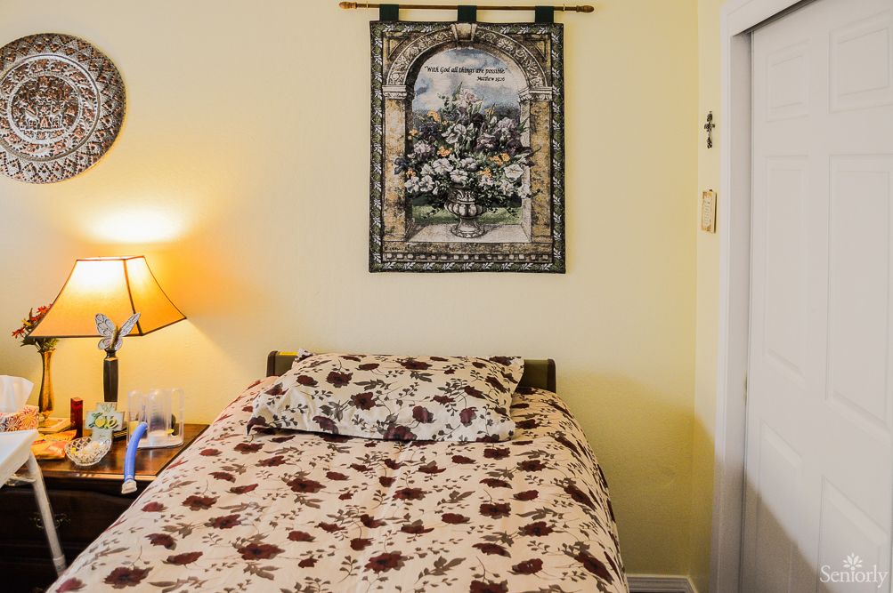 A cozy bedroom featuring a bed with patterned bedding, a bedside lamp, and a tapestry hanging on the wall.