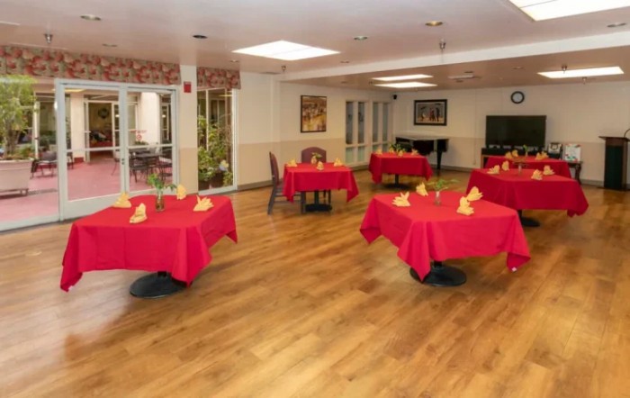 A dining area with red tablecloths on each table and a wooden floor, arranged in a cozy setting.