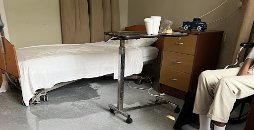A bedside table in a hospital room, featuring a clean bed and some items on the table.