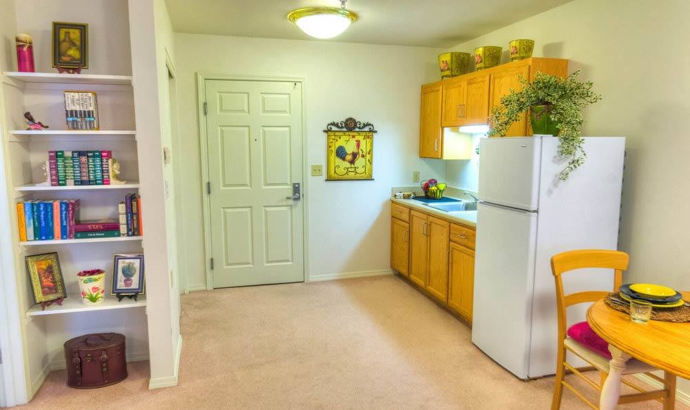 A cozy apartment kitchen with wooden cabinets, a white fridge, and decorative plants.