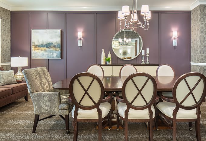 A beautifully decorated dining room featuring elegant chairs and a wooden table, complete with a chandelier and wall-mounted mirror.