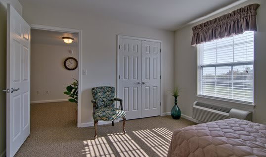 A cozy bedroom with a patterned chair, closet doors, and a window letting in natural light.
