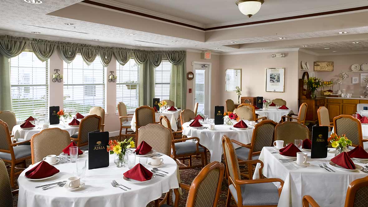 An elegant dining room with tables set for a meal, featuring white tablecloths and red napkins.
