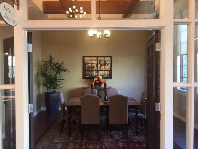 A cozy dining room with a wooden table, surrounded by upholstered chairs and illuminated by elegant ceiling lights.
