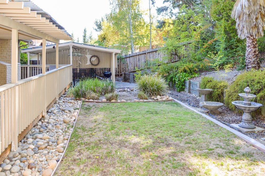 A well-maintained backyard with a grassy lawn, patio area, and various plants and trees.