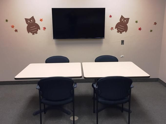 A small meeting room with tables, chairs, and a television, decorated with owl wall art.