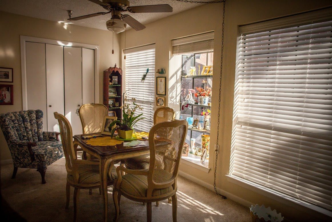 A cozy dining room bathed in sunlight, featuring a table with chairs and large windows with blinds.