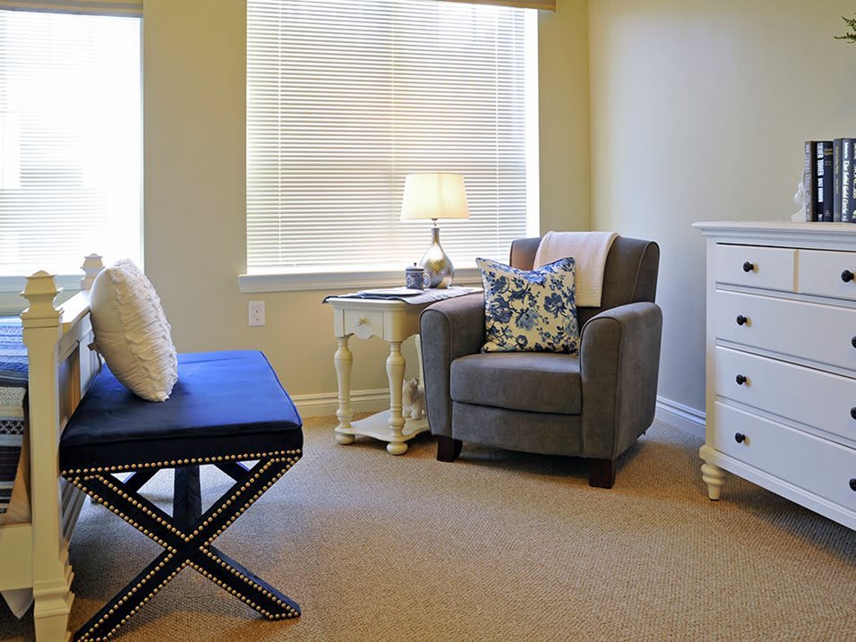 A cozy living room corner with a comfortable armchair, side table, lamp, and decorative pillows.