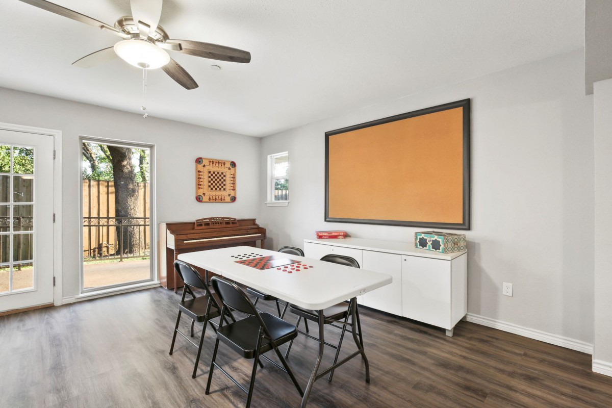 A modern dining area with a folding table and chairs, featuring a piano against the wall and a large window providing natural light.