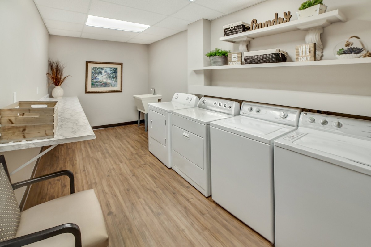 A neatly organized laundry room with washers, dryers, and shelves on a wooden floor.