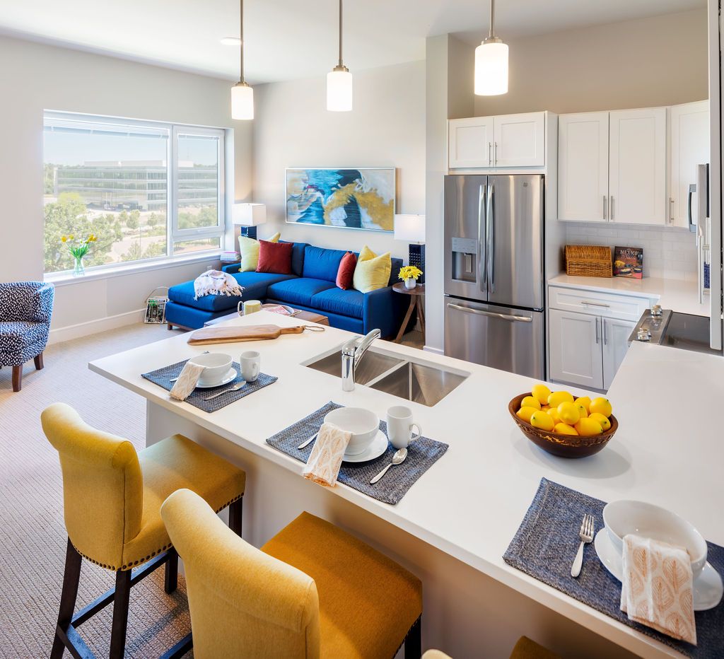 A modern open-concept kitchen and living room with bright lighting, featuring an island counter and stainless steel appliances.