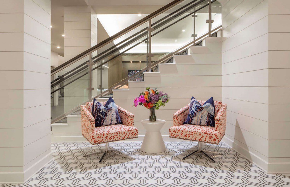 A modern seating area with two stylish chairs and a small table adorned with a floral arrangement, set beside a contemporary staircase.