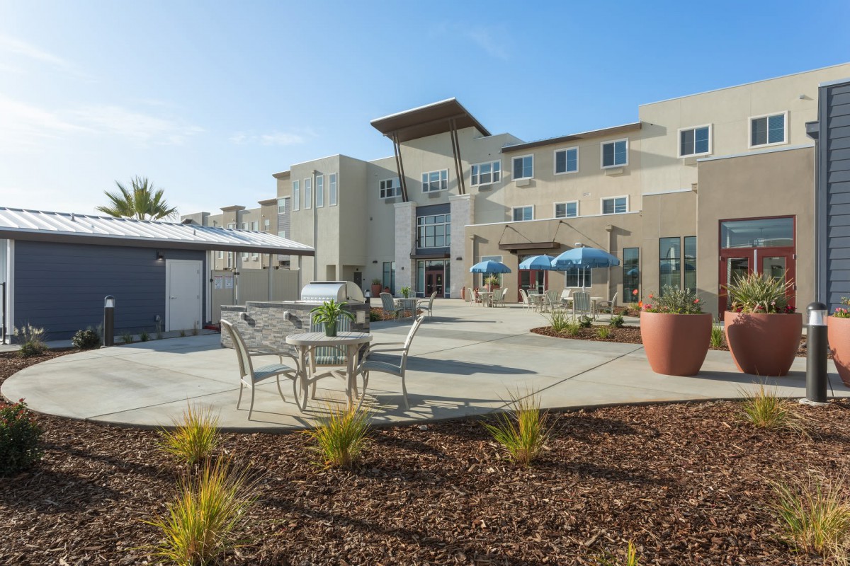 A modern building with a landscaped patio and outdoor furniture under a clear blue sky.