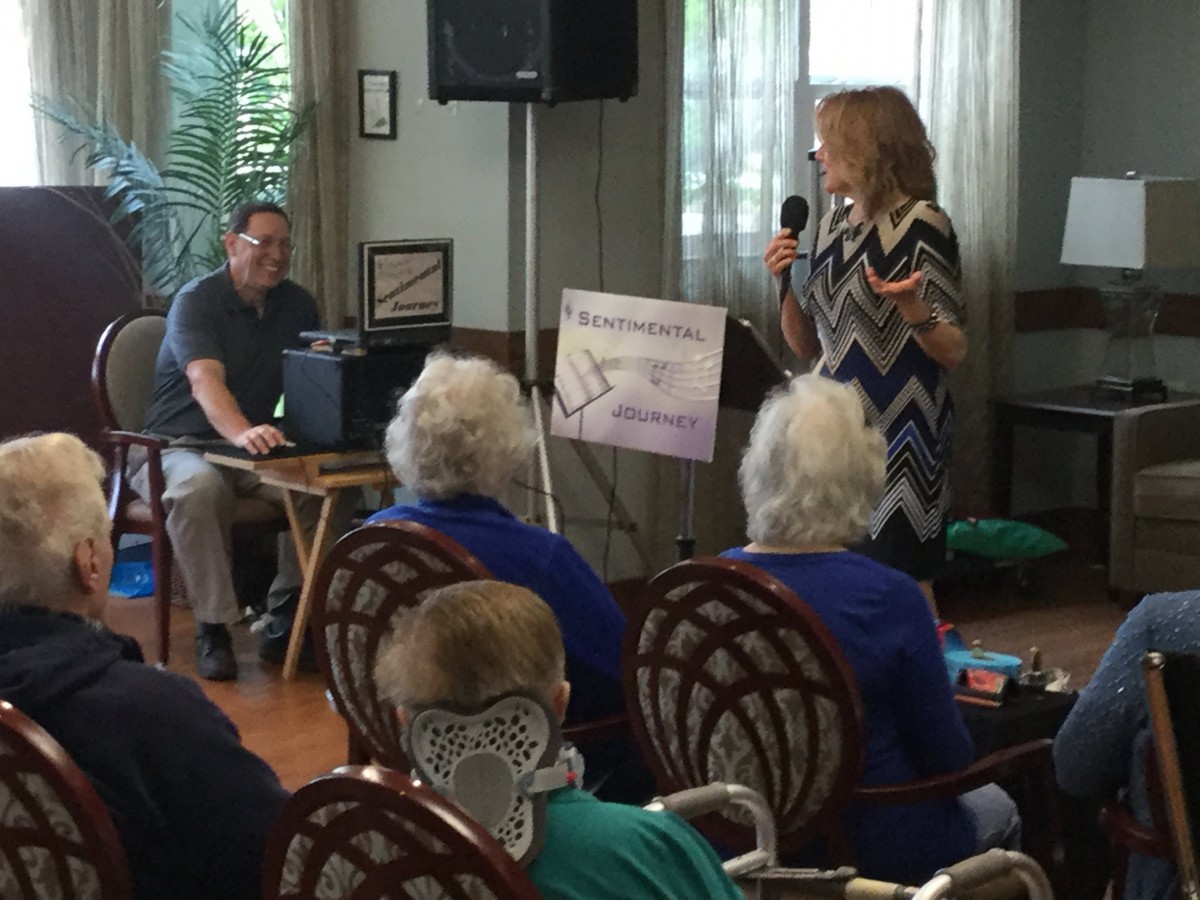 A speaker addresses an audience of elderly individuals at an indoor event.