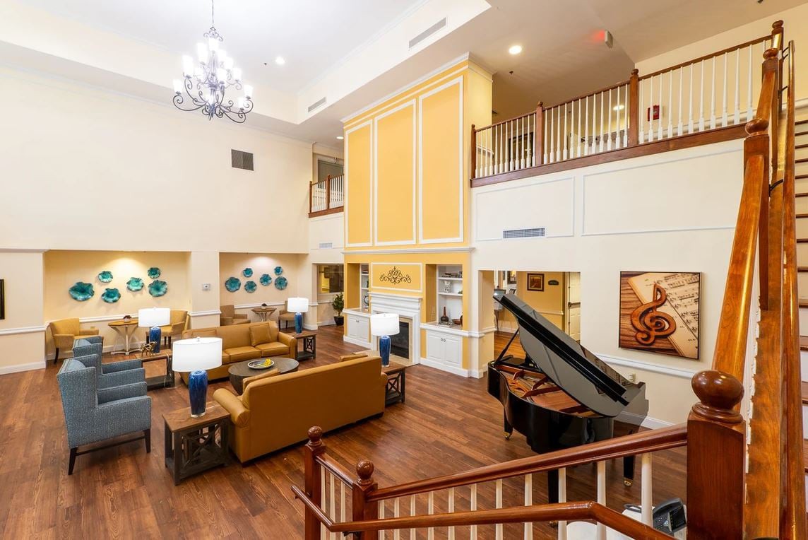 A spacious and elegantly designed lounge area featuring a grand piano, comfortable seating, and a chandelier.