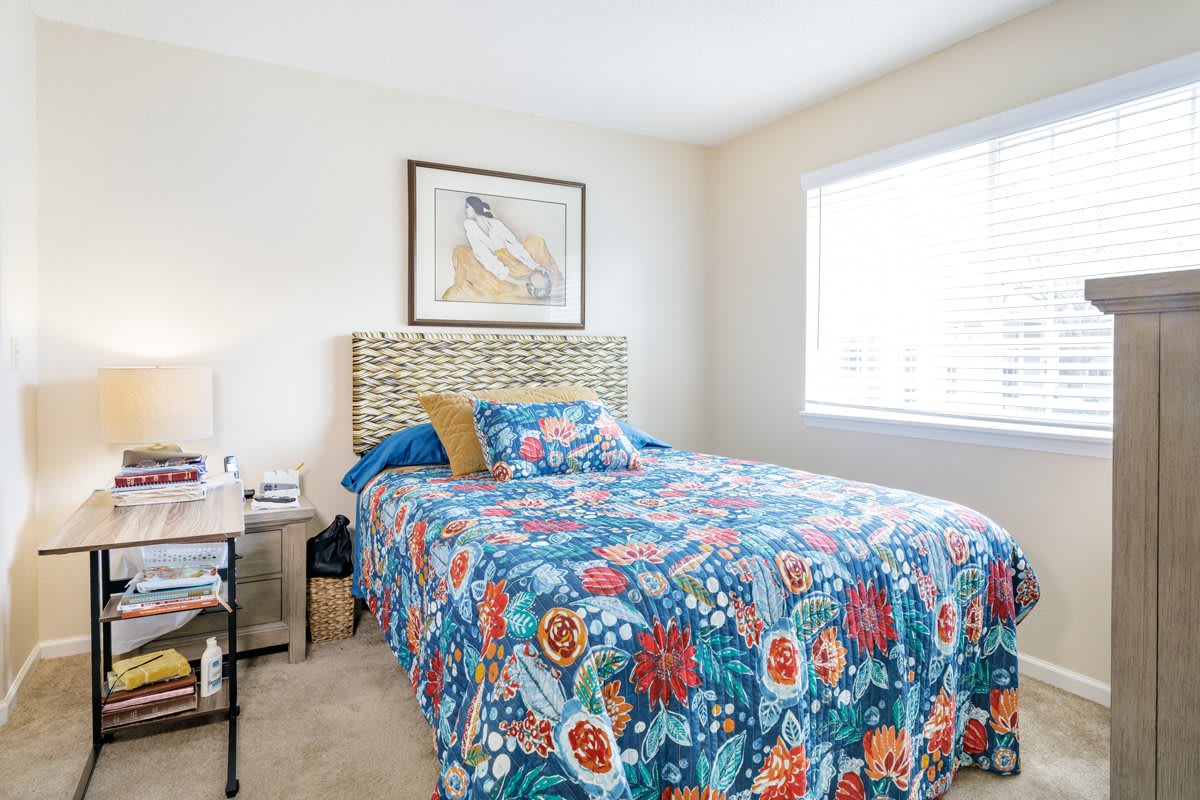 A bright bedroom with colorful floral bedding and a decorative headboard.