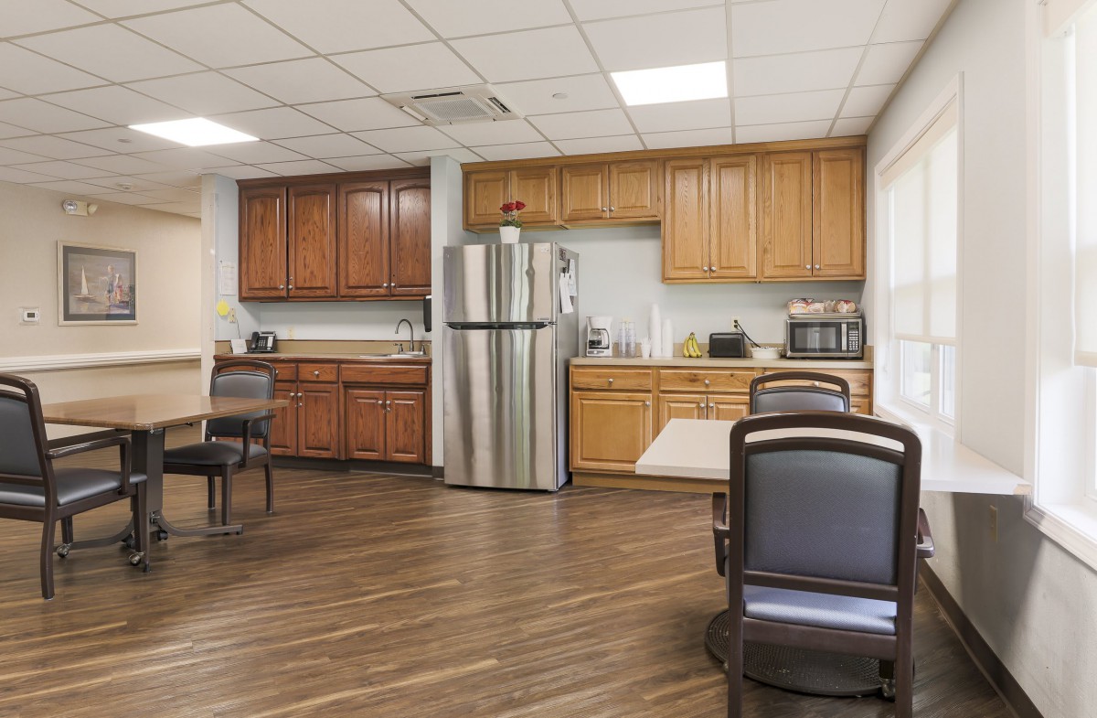 A spacious break room with wooden cabinets, a stainless steel refrigerator, and seating area.