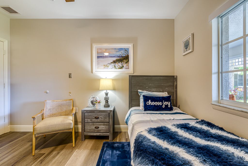 A cozy modern bedroom featuring a single bed with a plush blue and white blanket, a nightstand with a lamp, and wall artwork adding to the room's charm.